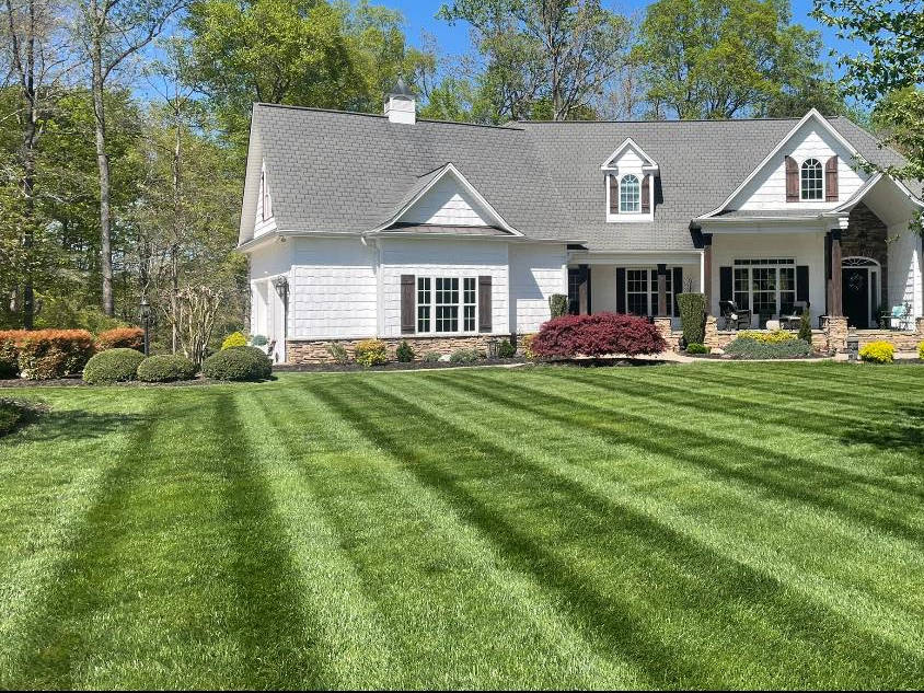Immaculately mowed lawn with striped patterns in front of an elegant white home with tasteful landscaping in Winston-Salem.